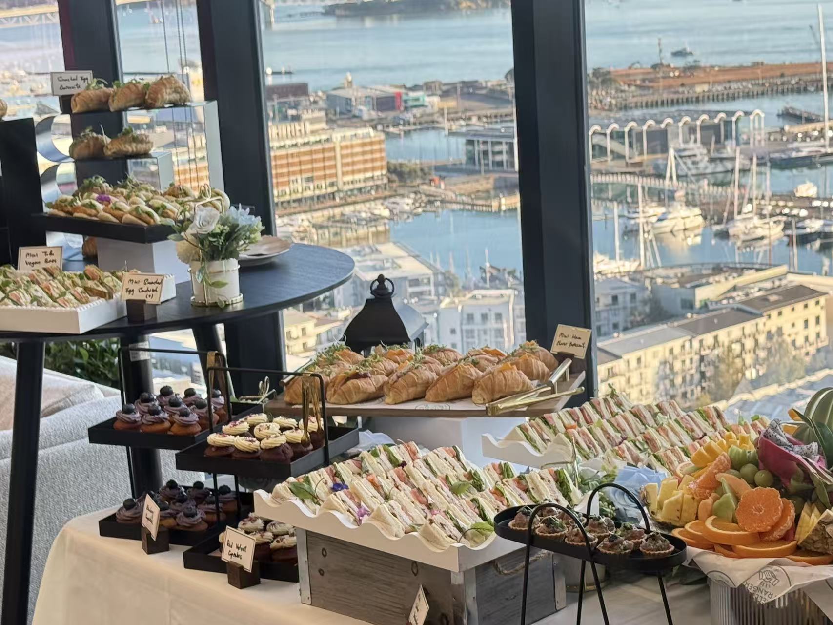 Grazing table with club sandwiches, croissants and cupcakes overlooking the marina
