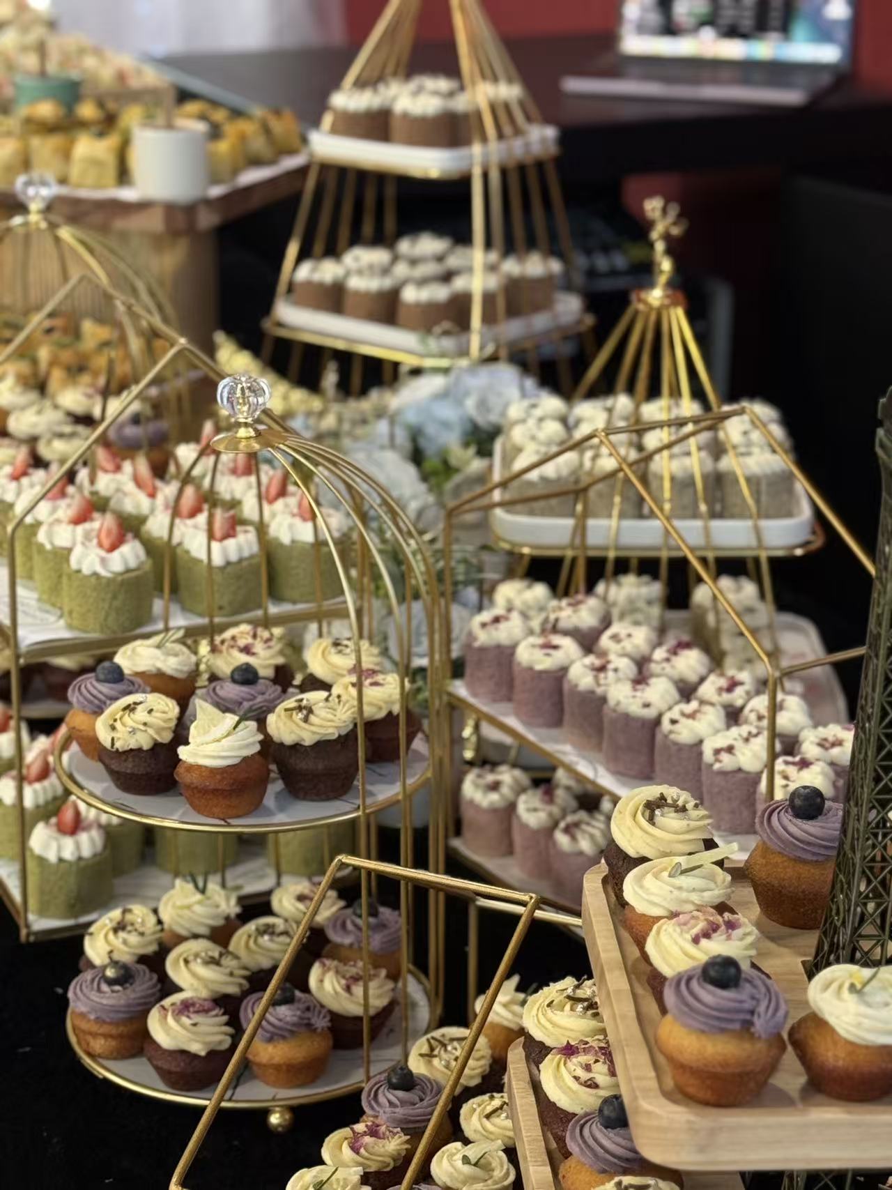 Dessert display of mini cupcakes, matcha slices and cakes on gold stands